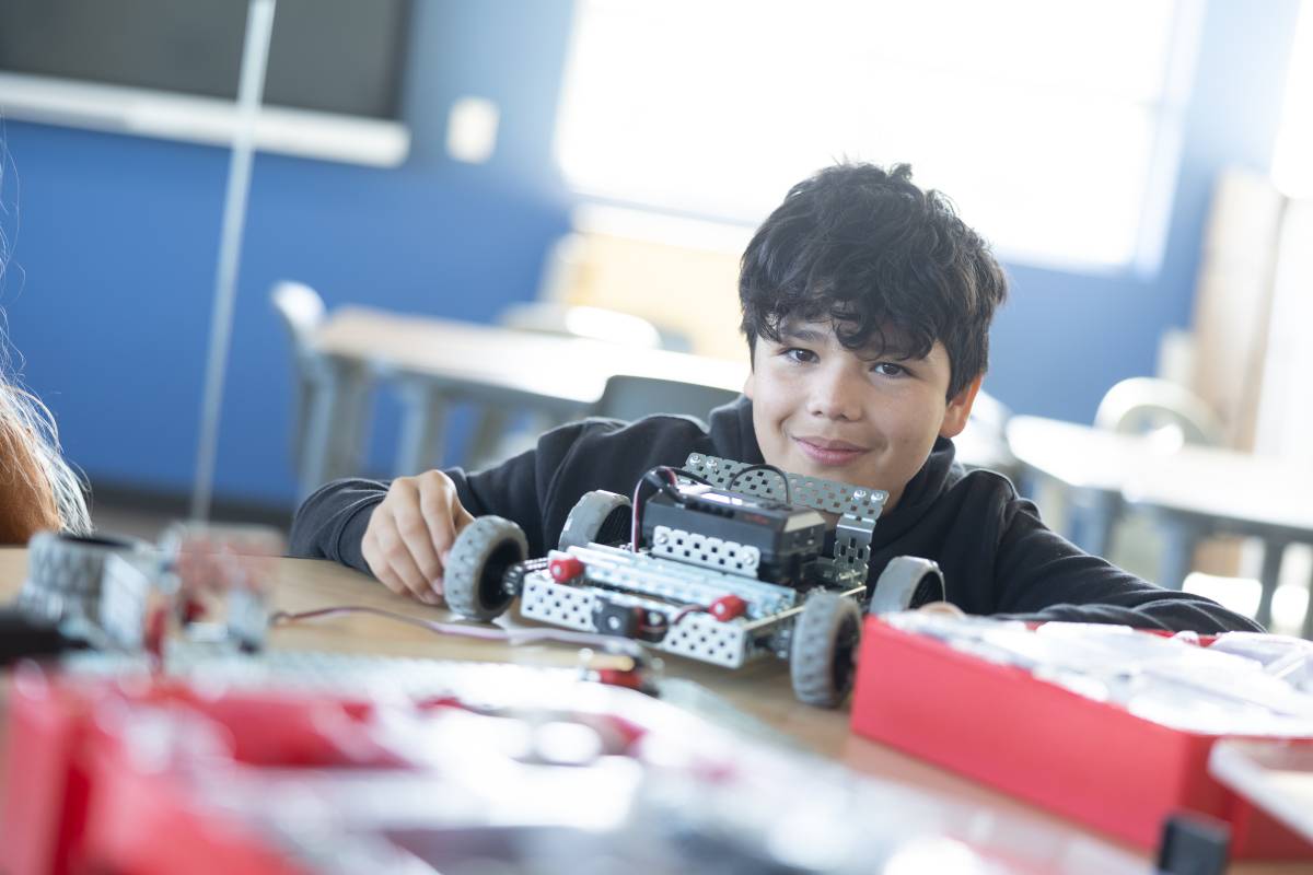 A SNACS student in a brightly lit classroom sitting at a table working on a hands-on robotics project.