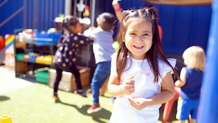 Pre-k student smiles while children play in background