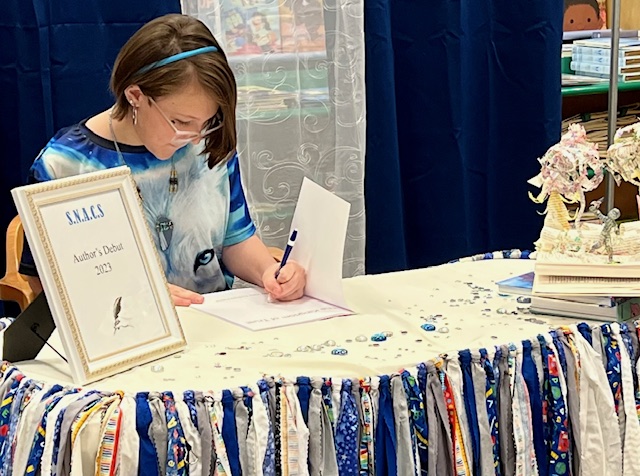 A SNACS student sitting at a table signing their published book at Barnes and Noble during the SNACS Author’s Debut event.