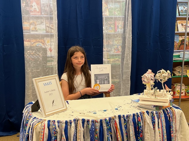 At the Author’s Debut, a SNACS student poses for a photo at a table in Barnes and Noble and shows off her hard work by displaying a book she authored!